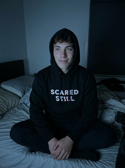Kevin in the SCARED STILL hoodie, hood up, in a dark bedroom