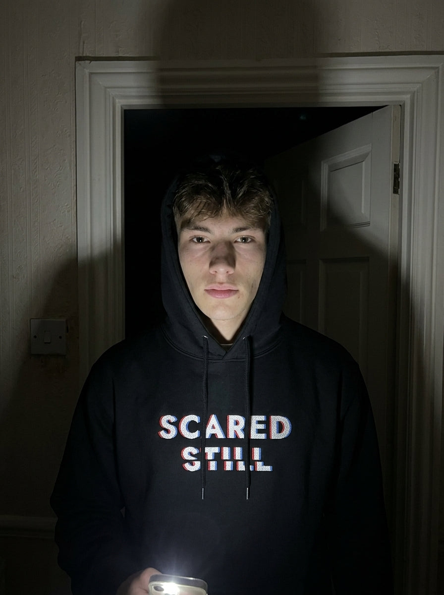 Kevin in the SCARED STILL hoodie in a dark hallway, lit by a phone torch