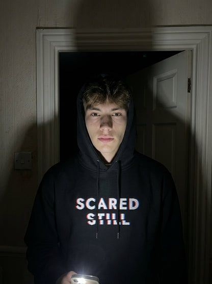 Kevin in the SCARED STILL hoodie in a dark hallway, lit by a phone torch